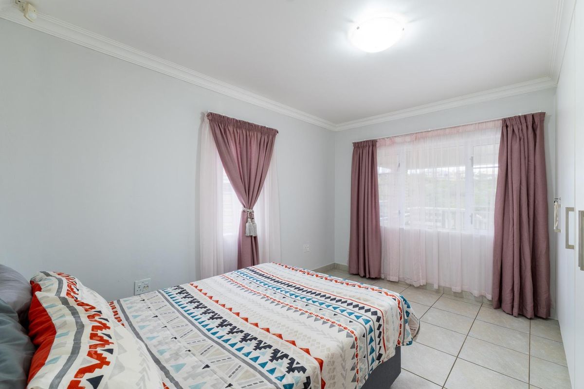 A bright bedroom featuring tiled flooring, built-in cupboards, and large windows with curtains, offering a clean and functional living space.