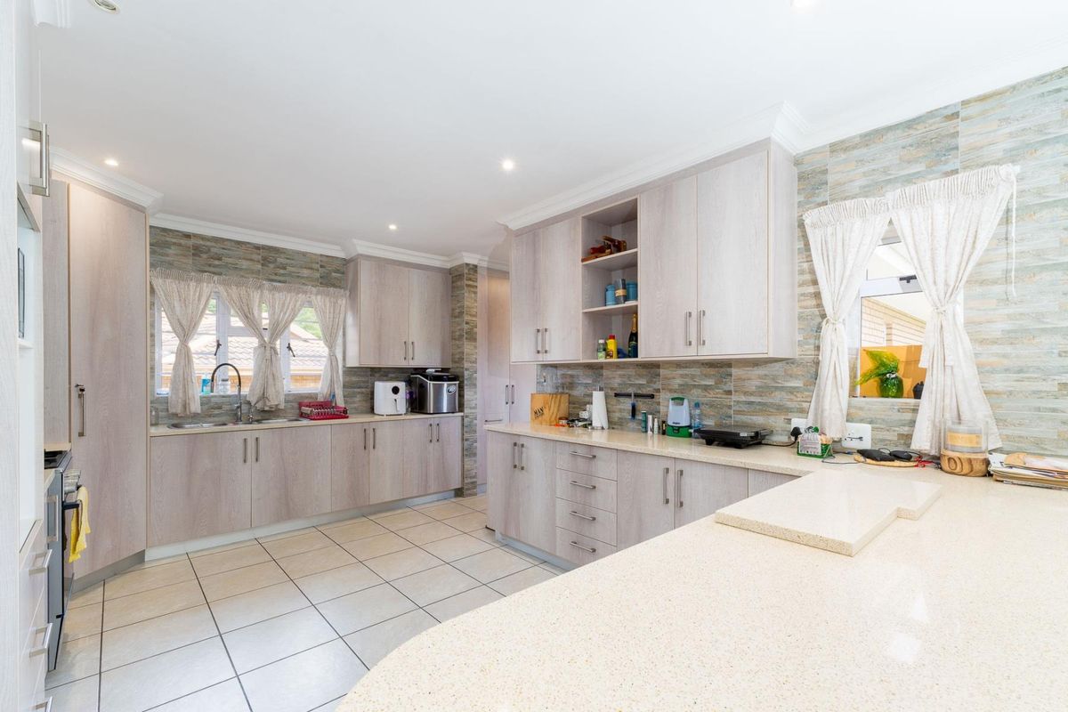 A well-maintained kitchen featuring light wood-grain cabinetry, stone-look tiled splashbacks, stone countertops, and a functional layout with ample storage space.