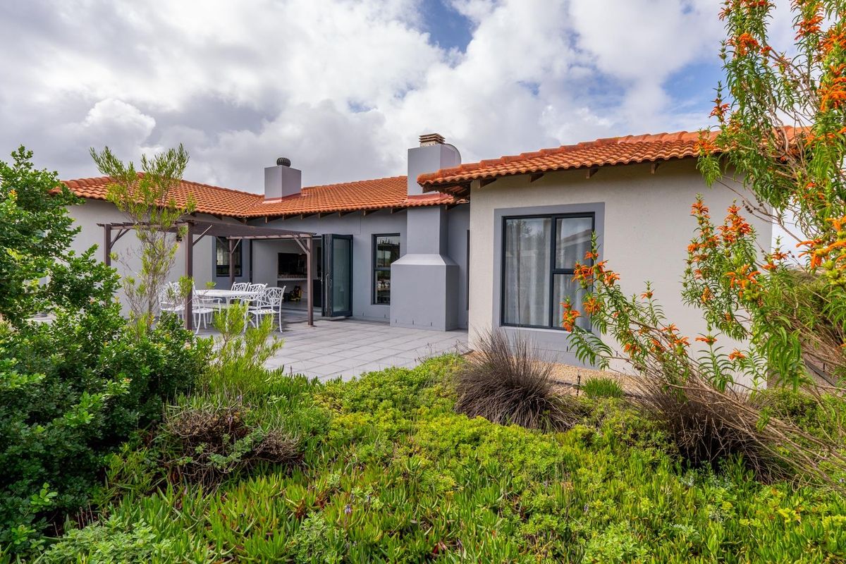 Rear view of the house featuring a paved patio area, built-in braai, terracotta roof tiles, and landscaped garden.