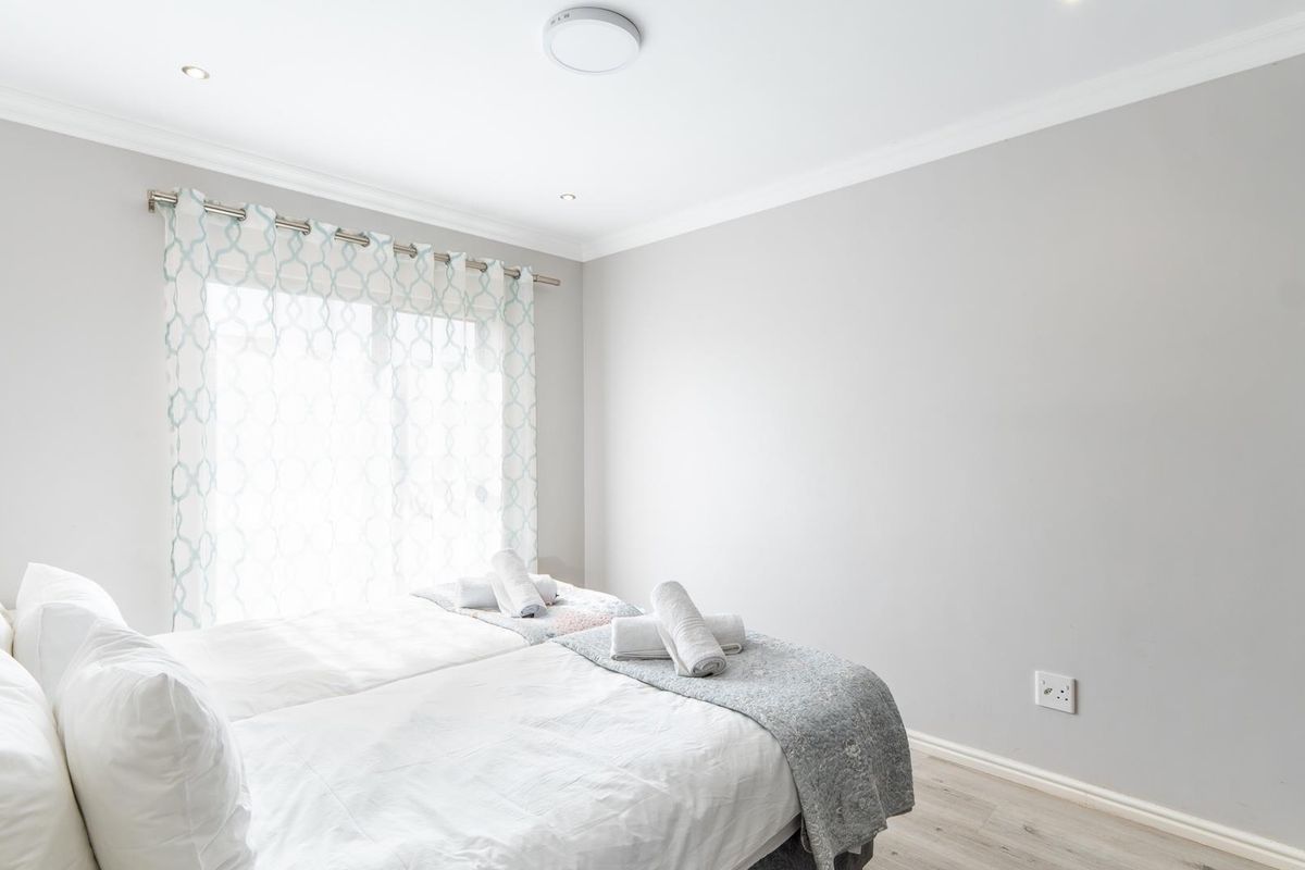 A bright and neutral bedroom featuring light wood-look flooring, built-in cabinetry, and large windows allowing for ample natural light.