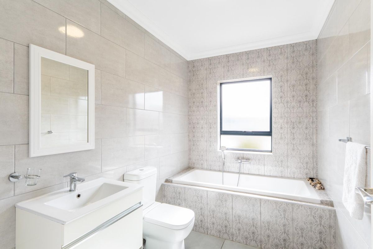 A modern, well-maintained bathroom featuring a built-in bathtub, a sleek vanity with a basin, and neutral wall tiling.