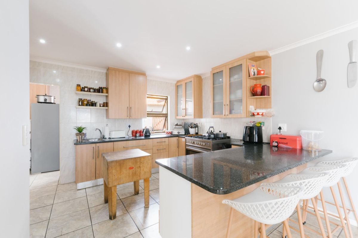 A functional kitchen featuring light wood cabinetry, dark granite countertops, a breakfast bar, and tiled flooring with an adjacent scullery area.