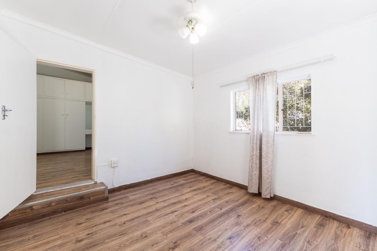 A bright, empty bedroom featuring wood-look laminate flooring, a ceiling fan, and a doorway leading to an adjacent room with built-in cabinetry.