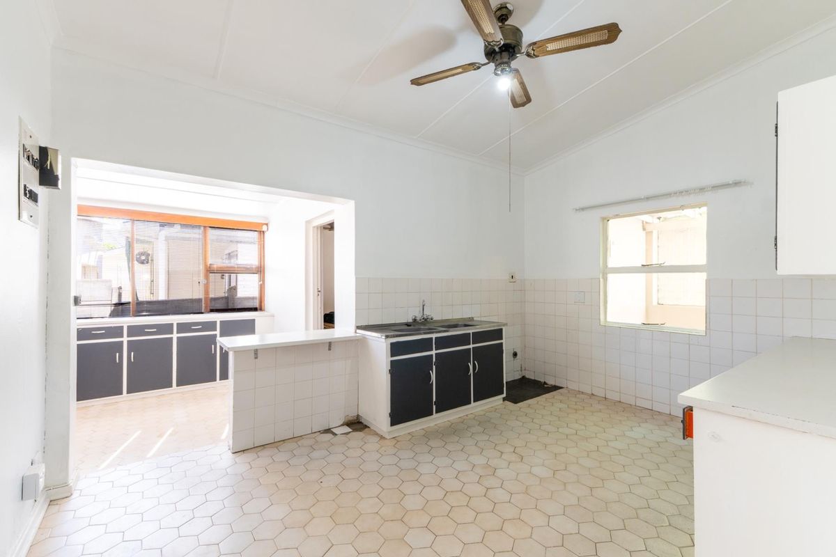 A dated kitchen featuring original cabinetry, tiled flooring, and a breakfast counter, offering a functional layout ready for modernization.