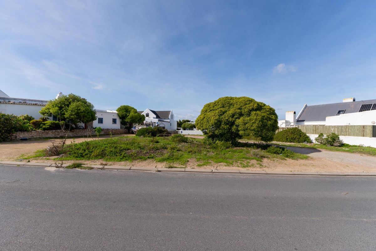 A view of the vacant residential plot from the street, featuring established greenery and surrounding residential properties.
