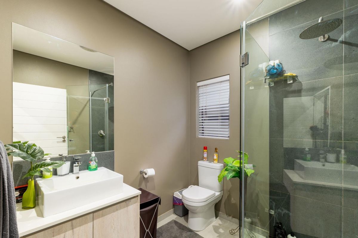 Modern bathroom featuring a glass-enclosed shower, contemporary vanity with basin, and a toilet, finished with neutral wall tones and tiled flooring.