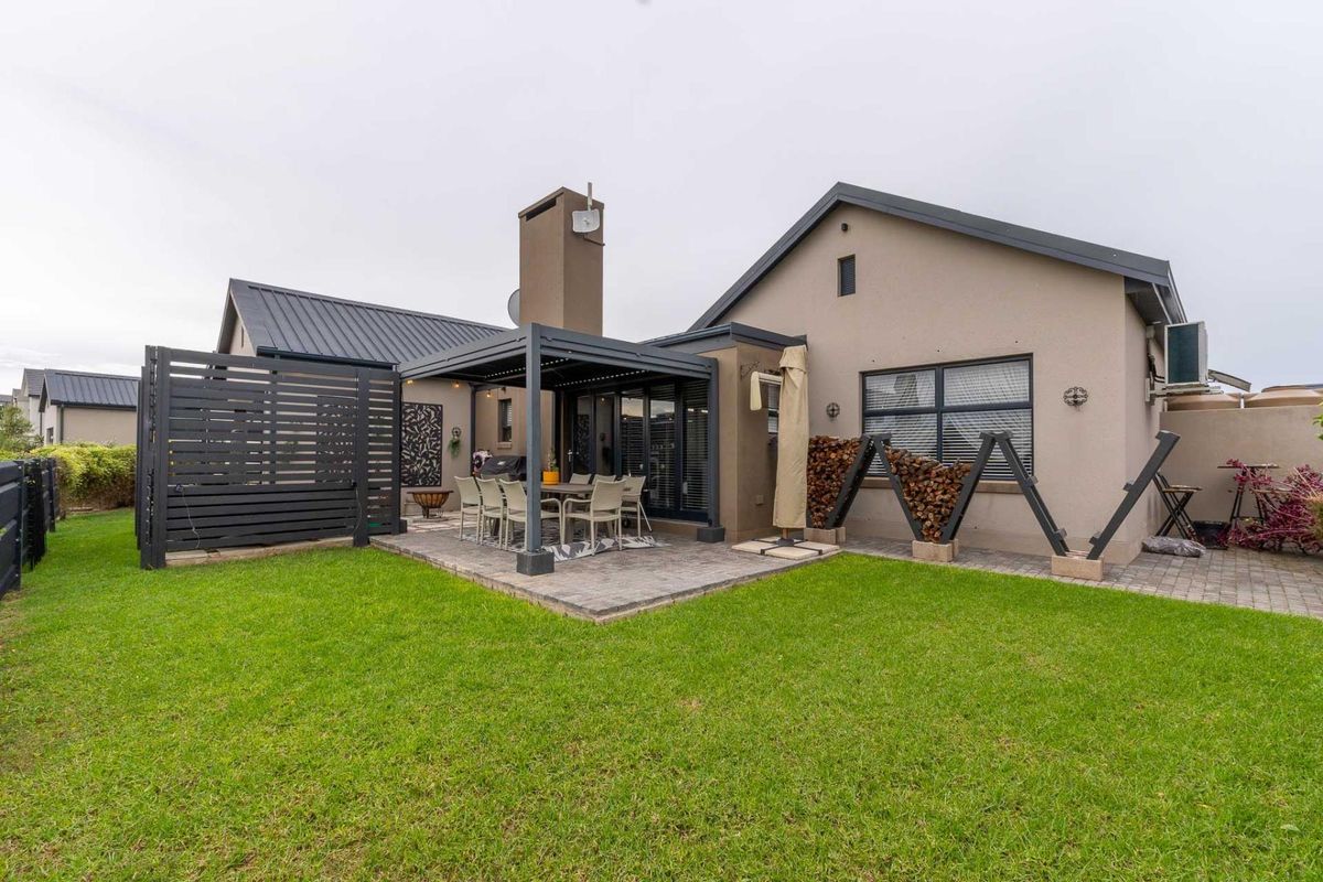 A well-maintained rear exterior featuring a paved patio area with a modern pergola, outdoor fireplace, and a neatly landscaped lawn.