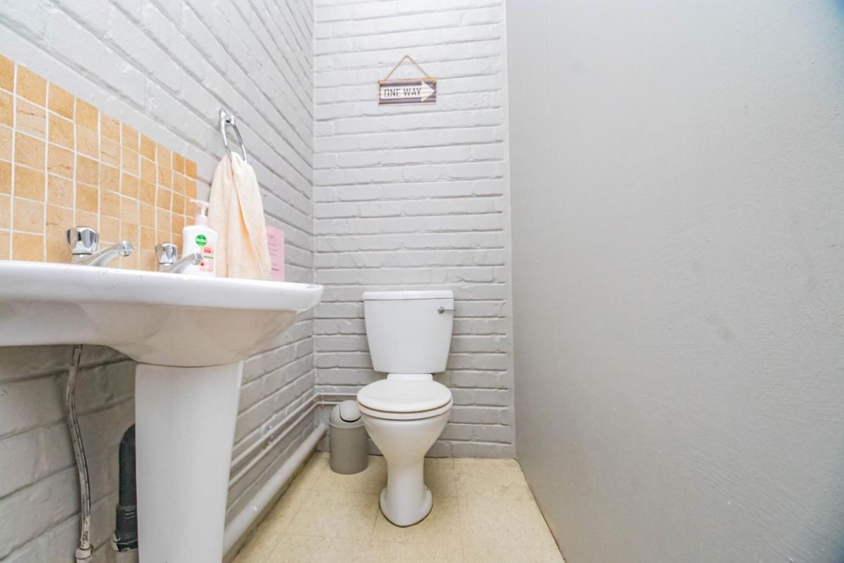 A compact office restroom featuring a pedestal sink with tiled splashback and a standard toilet against a painted brick wall.