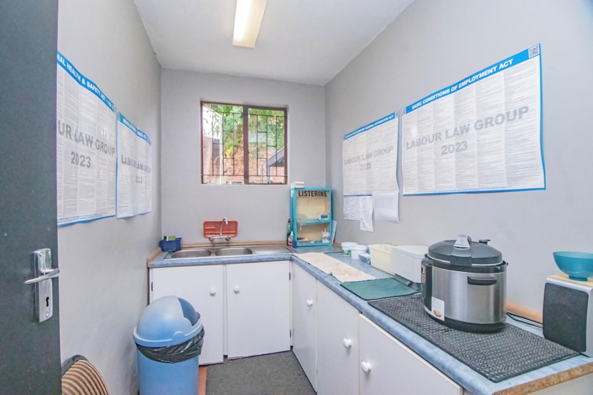 A functional office kitchenette featuring built-in cabinetry, a double sink, and a window with security bars.