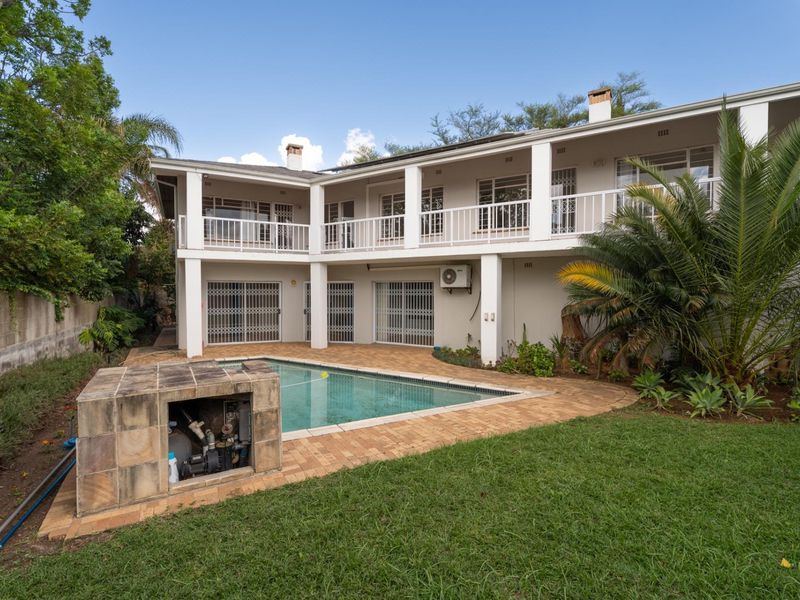 Rear view of the property featuring a swimming pool, paved patio area, and a two-story structure with a covered balcony and ground-floor patio.