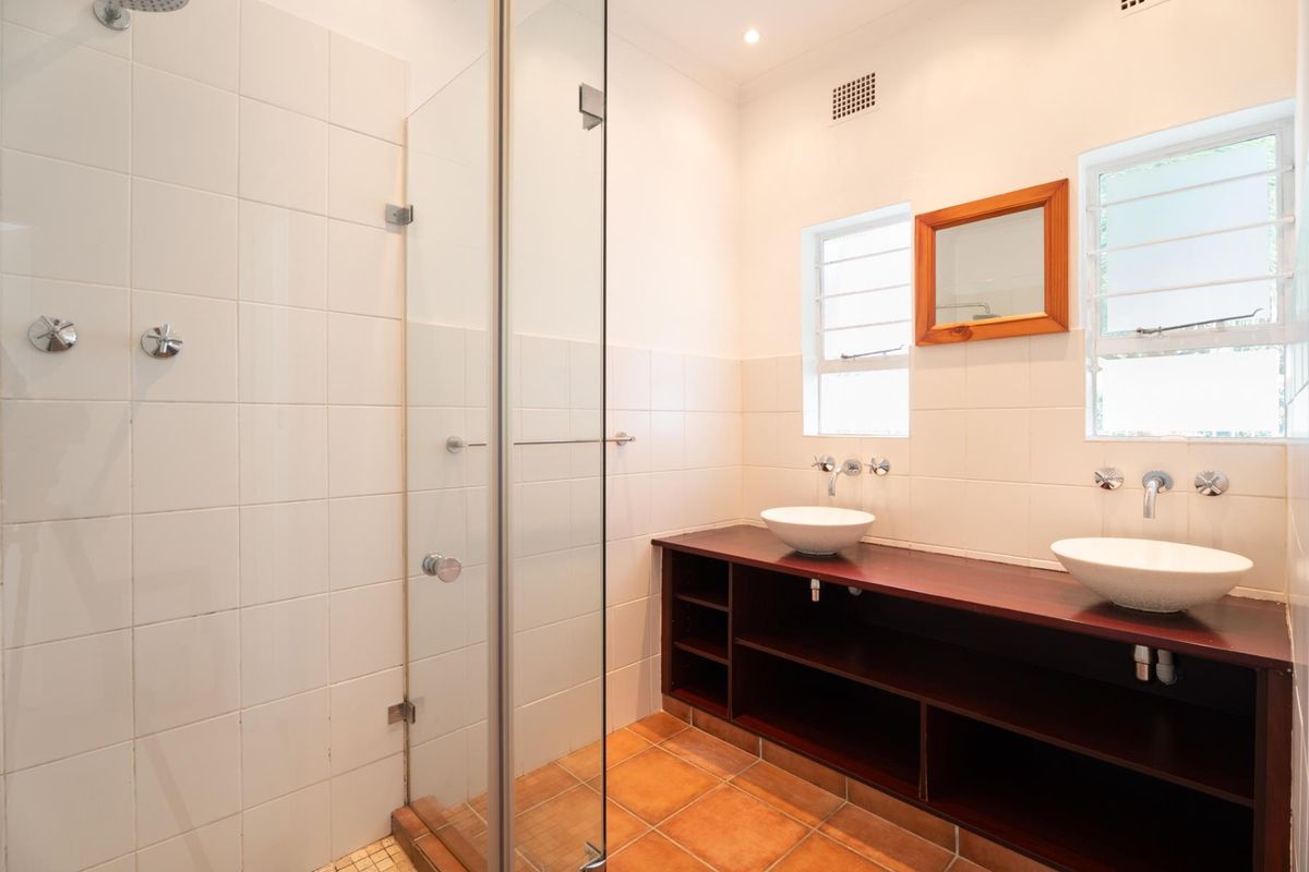 A clean, functional bathroom featuring a glass-enclosed shower, double vessel sinks on a dark wood vanity, and tiled finishes throughout.