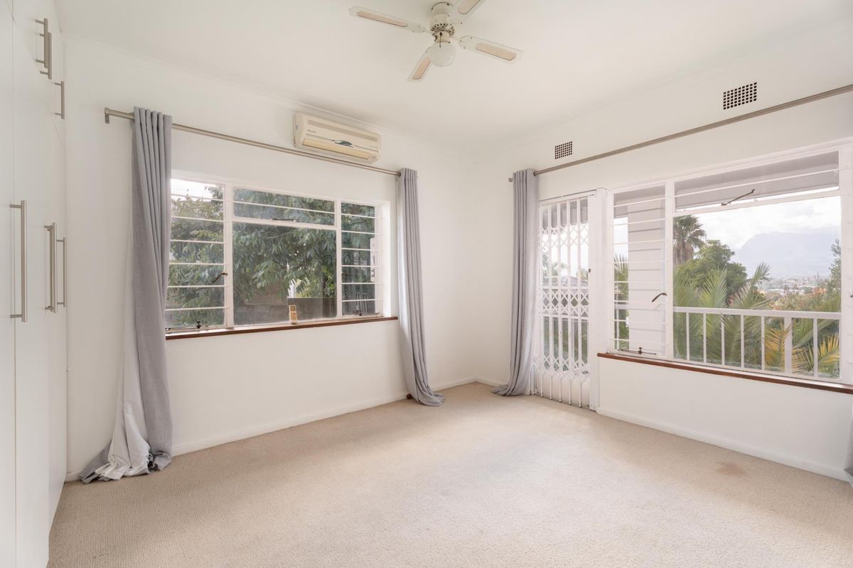 A bright, empty bedroom featuring built-in cupboards, a ceiling fan, air conditioning, and direct access to an outdoor area through a security gate.