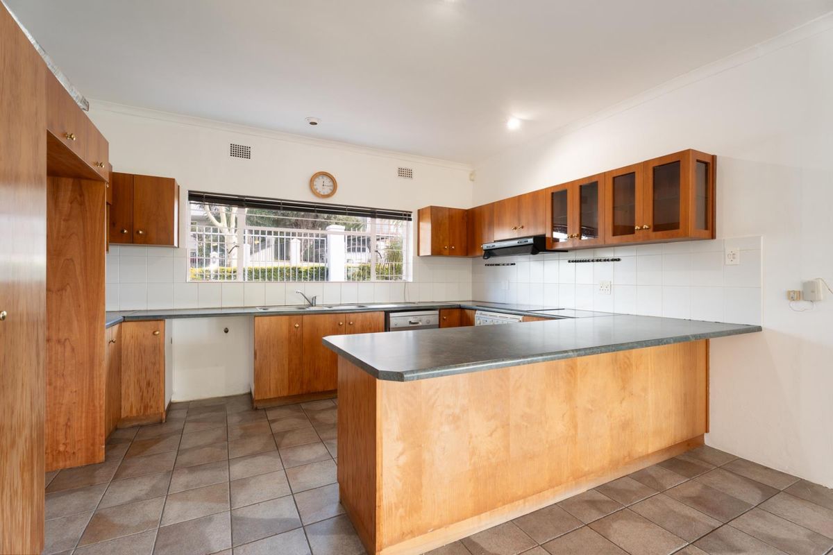 A spacious, empty kitchen featuring wooden cabinetry, laminate countertops, tiled flooring, and a functional layout with a breakfast bar area.