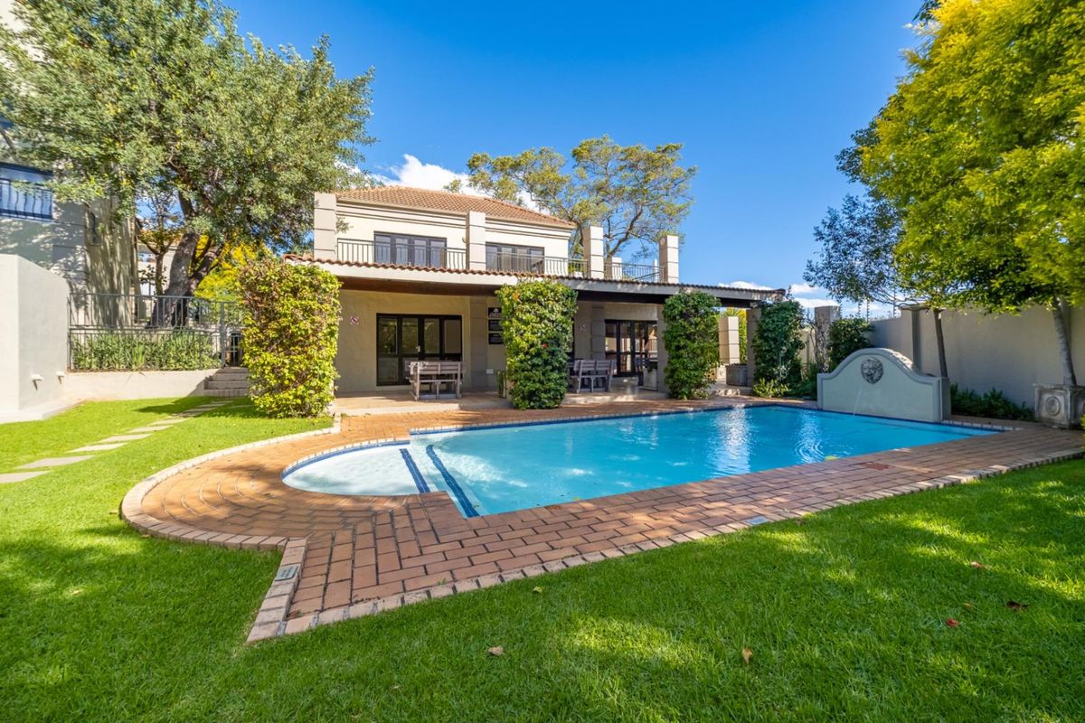 A well-maintained rear exterior view featuring a swimming pool with brick paving, a covered patio, and a landscaped garden area.