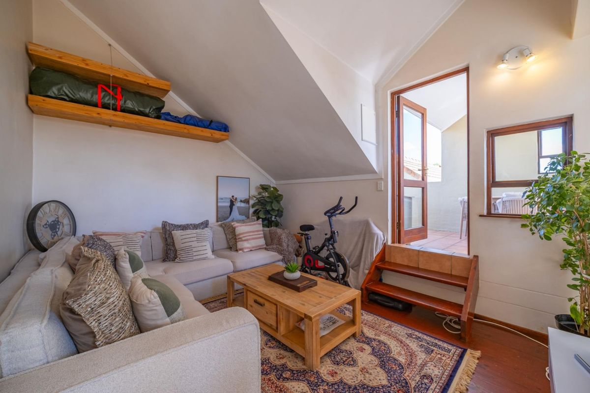 A cozy living room featuring sloped ceilings, wooden shelving, and direct access to an outdoor balcony area.