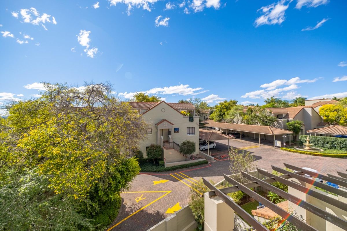 Elevated view of the apartment complex grounds, featuring paved driveways, covered parking bays, and landscaped garden areas.