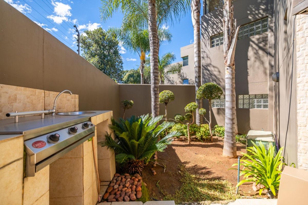 Private rear courtyard featuring a built-in gas braai, stainless steel sink, stone-clad prep area, and established garden landscaping.