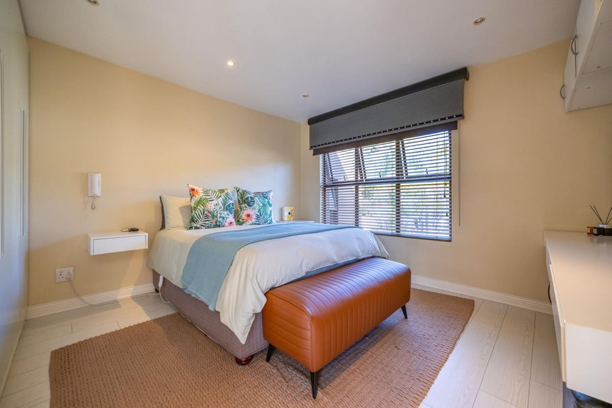 A well-maintained bedroom featuring laminate flooring, recessed lighting, built-in cupboards, and a floating bedside shelf with venetian blinds.
