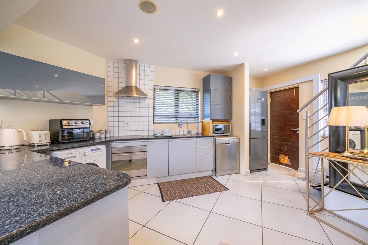Functional kitchen featuring granite countertops, stainless steel appliances, tiled flooring, and an adjacent staircase with modern metal railing.