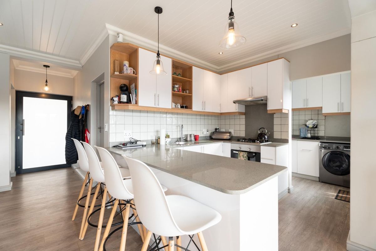 Modern kitchen featuring white cabinetry, stone countertops, a breakfast bar, integrated gas hob, and tiled backsplash, seamlessly flowing into the living area.