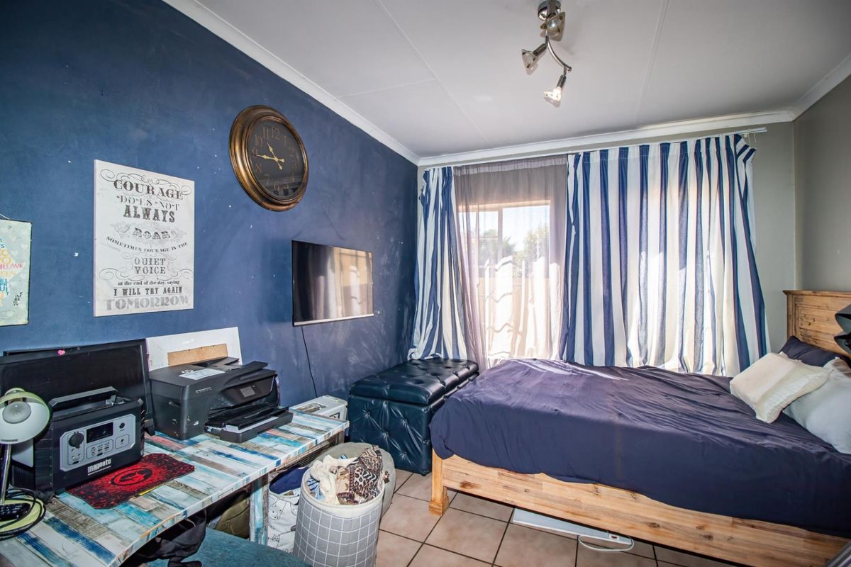 A bedroom featuring tiled flooring, a large window with curtains, and a wall-mounted television.