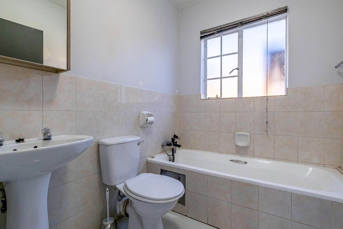 A functional bathroom featuring a pedestal basin, toilet, and bathtub with tiled walls and flooring, offering a clean and practical layout.