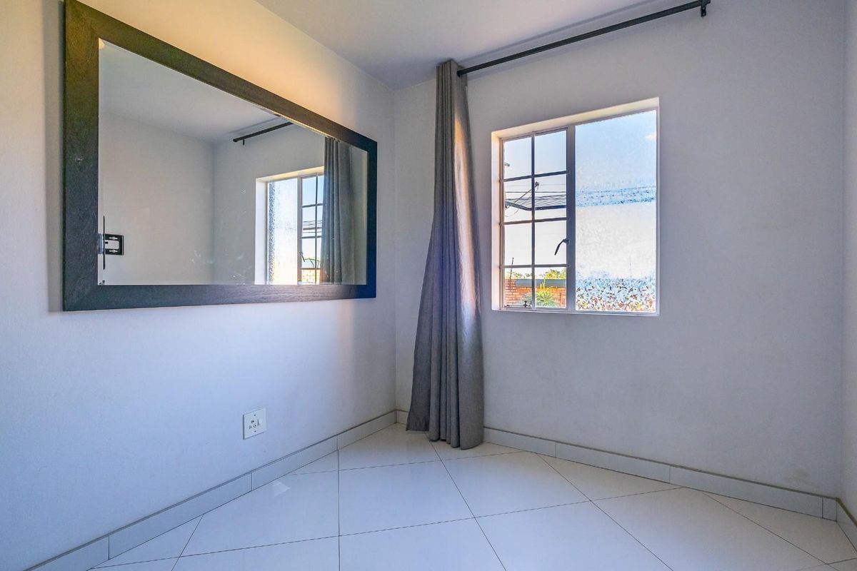 A bright, empty bedroom featuring clean tiled flooring, a window with a curtain rod, and neutral wall finishes.