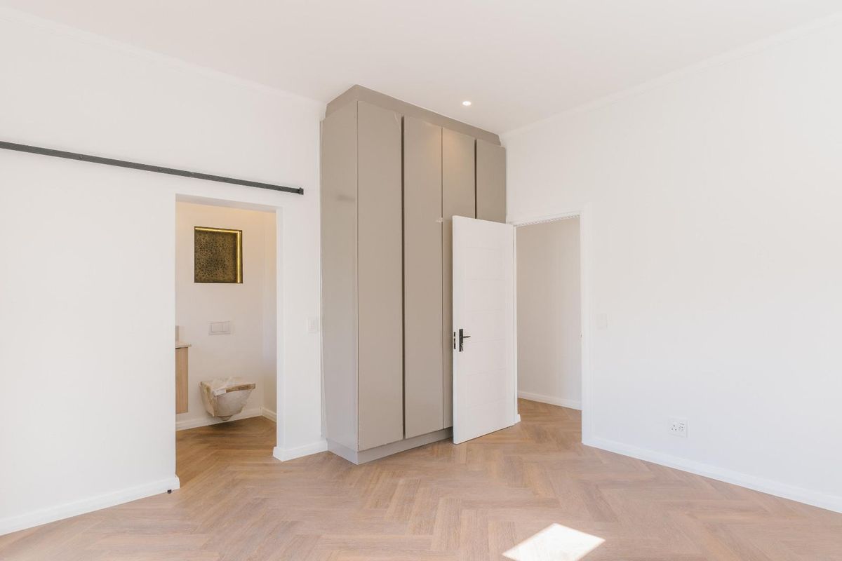 A bright, empty bedroom featuring modern herringbone timber flooring, built-in cupboards, and an en-suite bathroom access point.