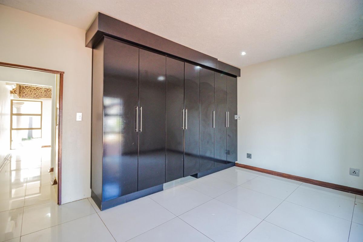 A bedroom featuring large, dark built-in cupboards with modern handles and polished floor tiles.