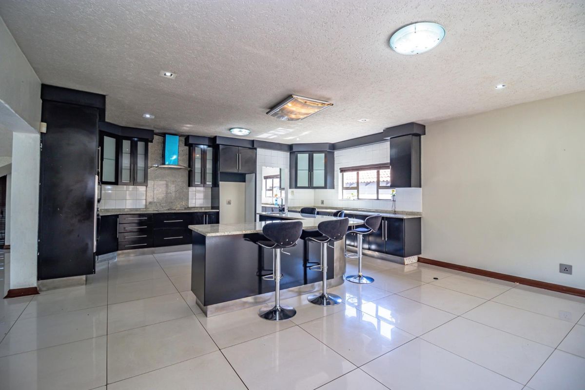 Spacious kitchen featuring dark cabinetry, granite countertops, a central island with breakfast bar seating, and tiled flooring.