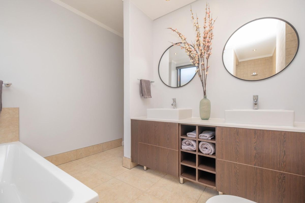 Modern bathroom featuring a double vanity with wood-finish cabinetry, vessel sinks, circular mirrors, and a separate bathtub.