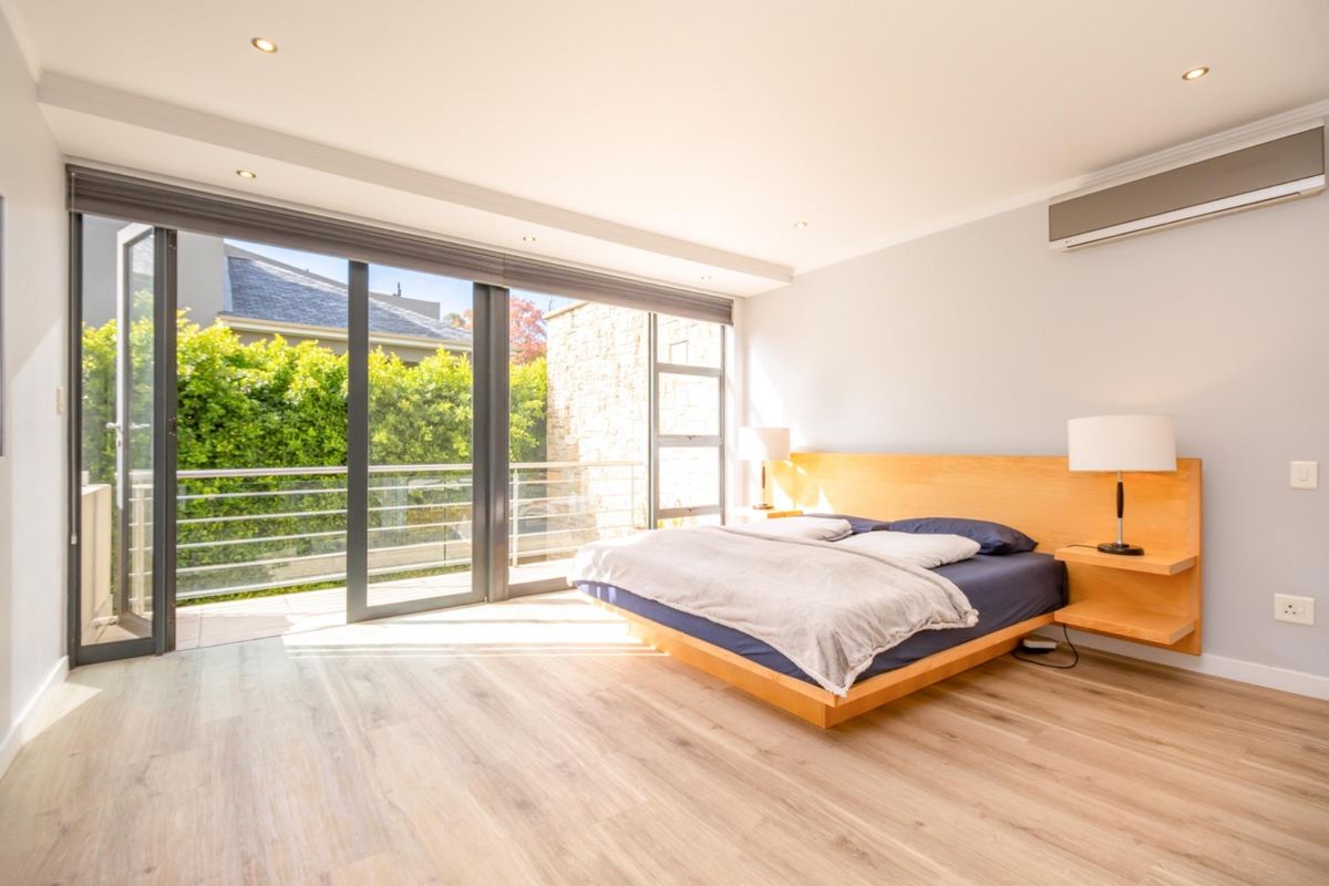 Spacious bedroom featuring light wood-look flooring, recessed ceiling lighting, a wall-mounted air conditioning unit, and large sliding glass doors opening to a private balcony.