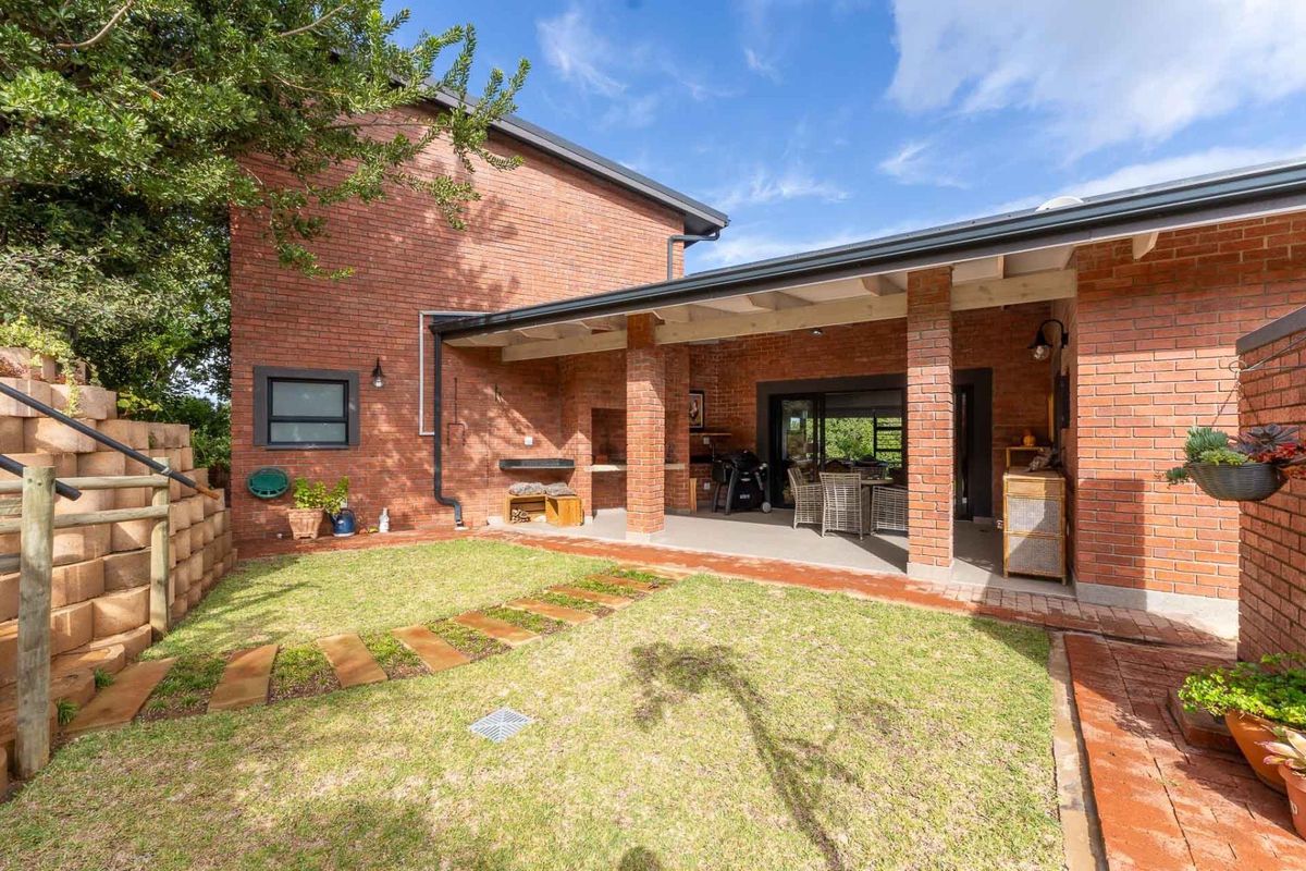 A well-maintained rear exterior featuring a covered patio with brick pillars, a built-in braai, and a landscaped garden with stone pavers.