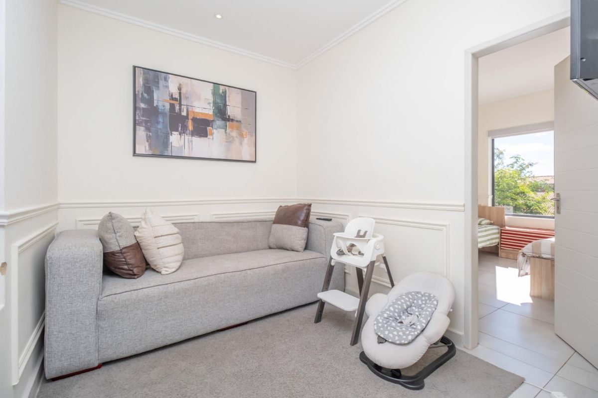A cozy living area featuring decorative wall wainscoting and neutral carpeting, with an open doorway leading to an adjacent bedroom.