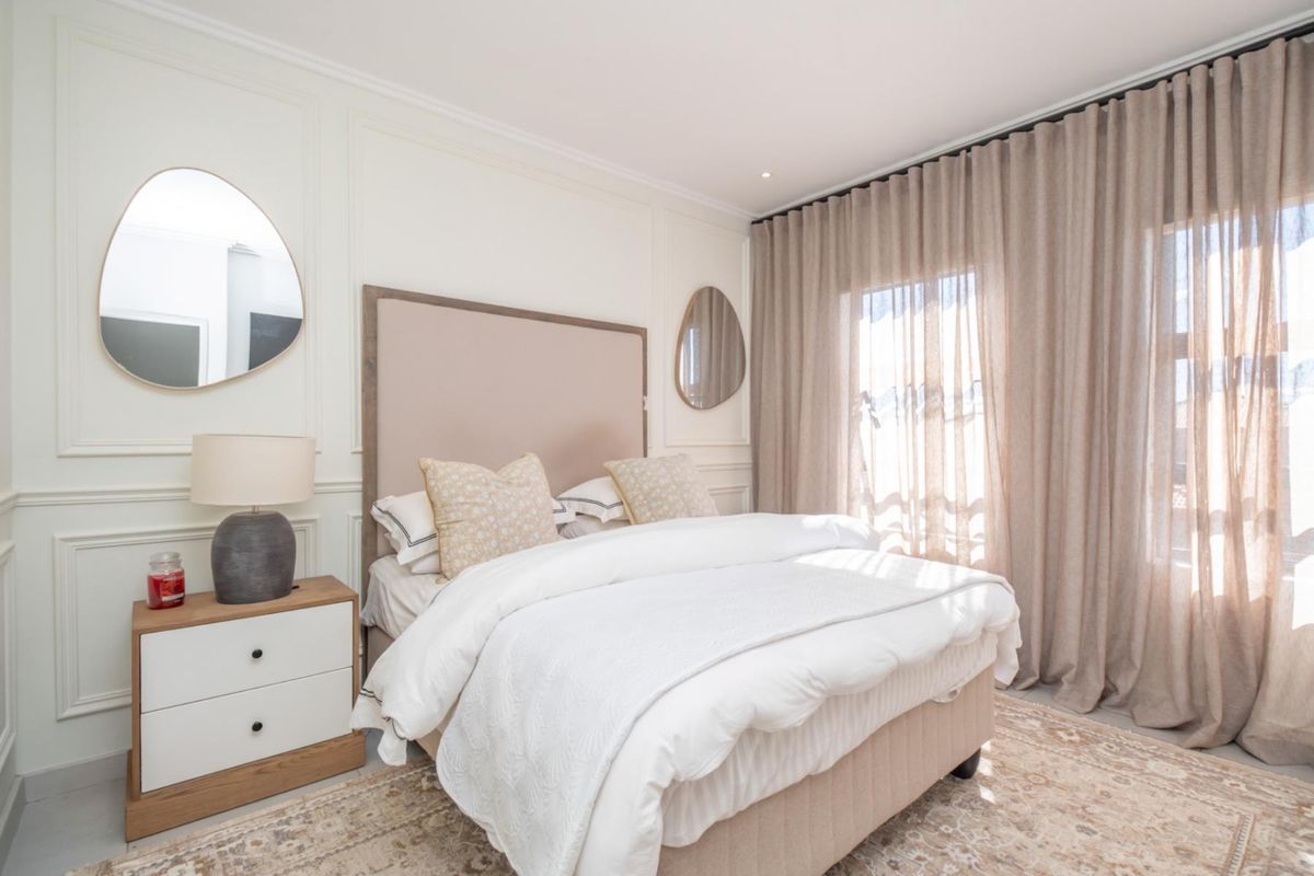 A well-appointed bedroom featuring elegant wall molding, recessed ceiling lighting, and floor-to-ceiling curtains providing natural light.