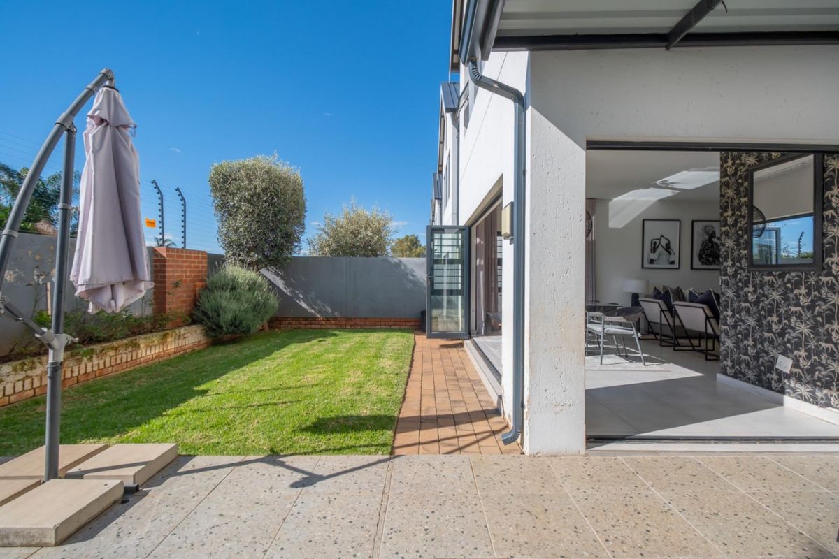 A well-maintained rear garden featuring a paved patio area, a small lawn, and seamless indoor-outdoor flow through large sliding doors.