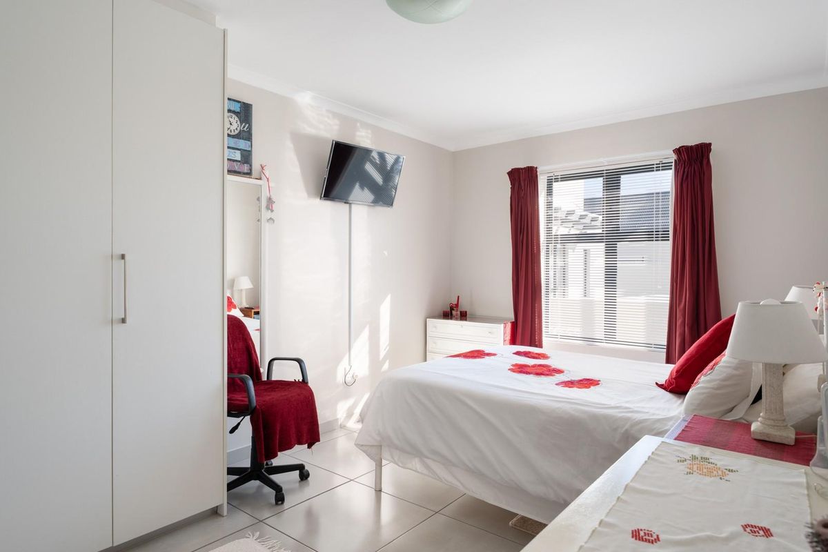 A bright bedroom featuring tiled flooring, built-in wardrobe cabinetry, and a window with fitted blinds.