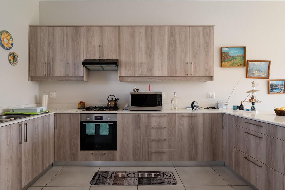 Modern U-shaped kitchen featuring light wood-grain cabinetry, stone countertops, integrated oven, gas hob, and stainless steel extractor fan.
