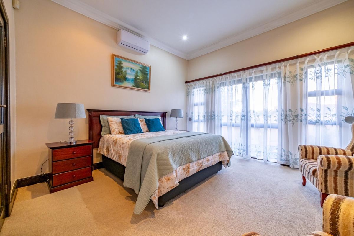 A well-maintained bedroom featuring neutral carpeting, crown molding, and a wall-mounted air conditioning unit, with large windows providing ample natural light.