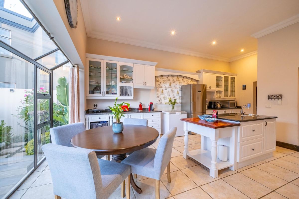 A bright kitchen featuring white cabinetry, a central island with a wooden countertop, tiled flooring, and large glass doors opening to a side garden.