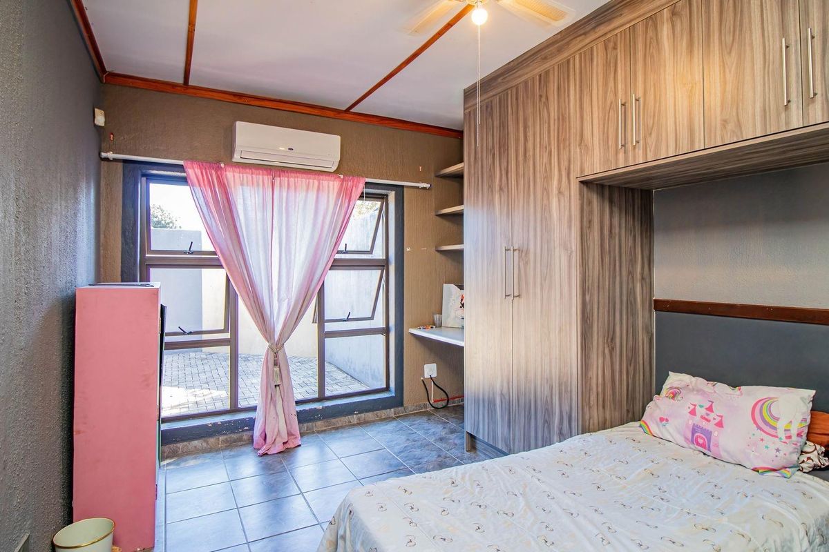 Bedroom featuring built-in wood-grain cabinetry, tiled flooring, wall-mounted air conditioning unit, and large windows providing natural light.