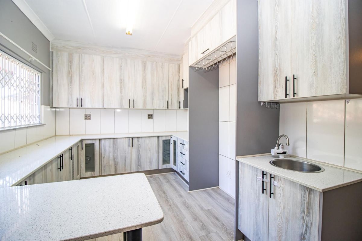 Modern kitchen featuring light wood-grain cabinetry, stone-look countertops, a stainless steel sink, and tiled splashbacks with ample storage space.