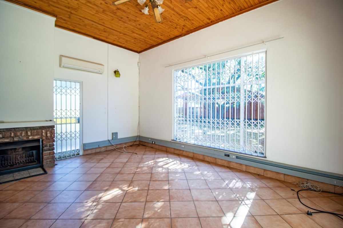 Spacious living room featuring a brick fireplace, tiled flooring, timber-clad ceiling, and security gates on windows and doors.