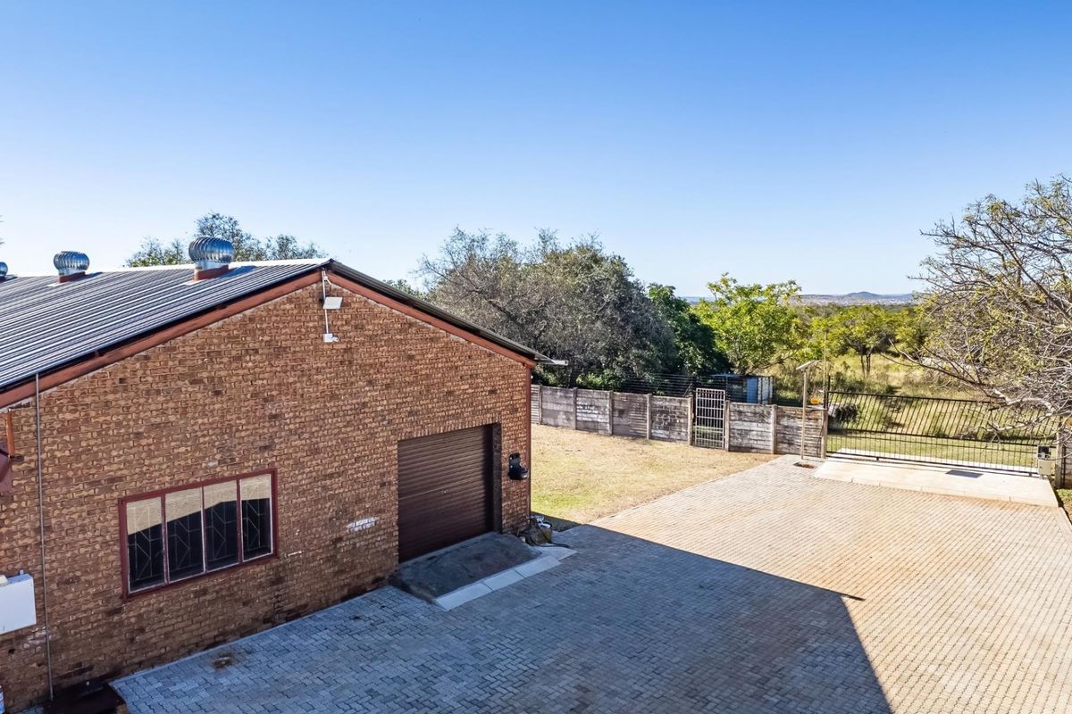 Aerial view of a brick farm building featuring a roller shutter garage door, metal roof with ventilation turbines, and a paved driveway area.