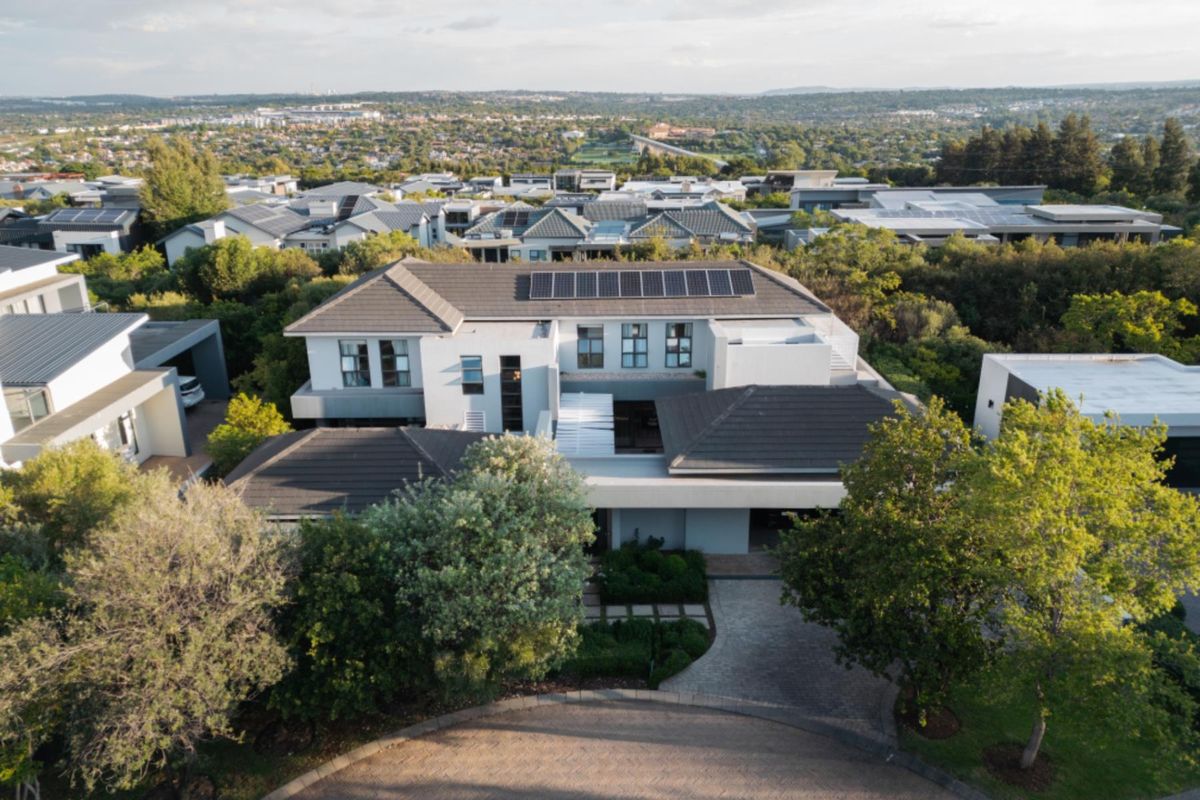 Aerial view of a modern residential property featuring a tiled roof with integrated solar panels, a paved driveway, and established garden landscaping.