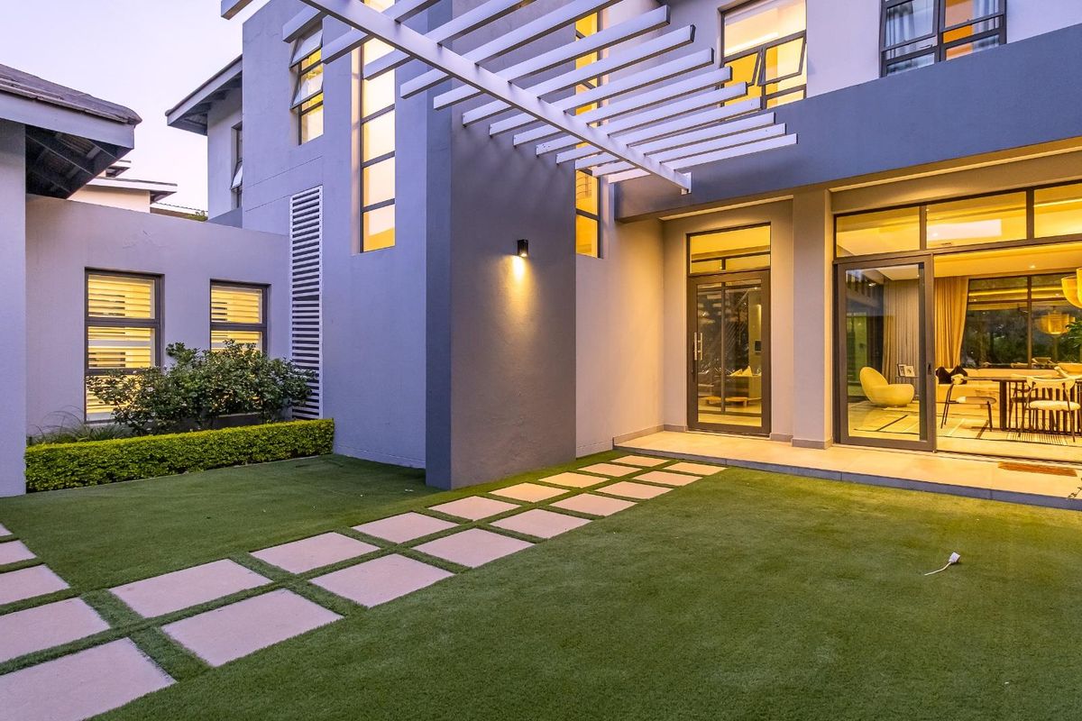 Modern rear exterior featuring a pergola, artificial lawn, paver walkway, and large sliding glass doors providing seamless indoor-outdoor flow.