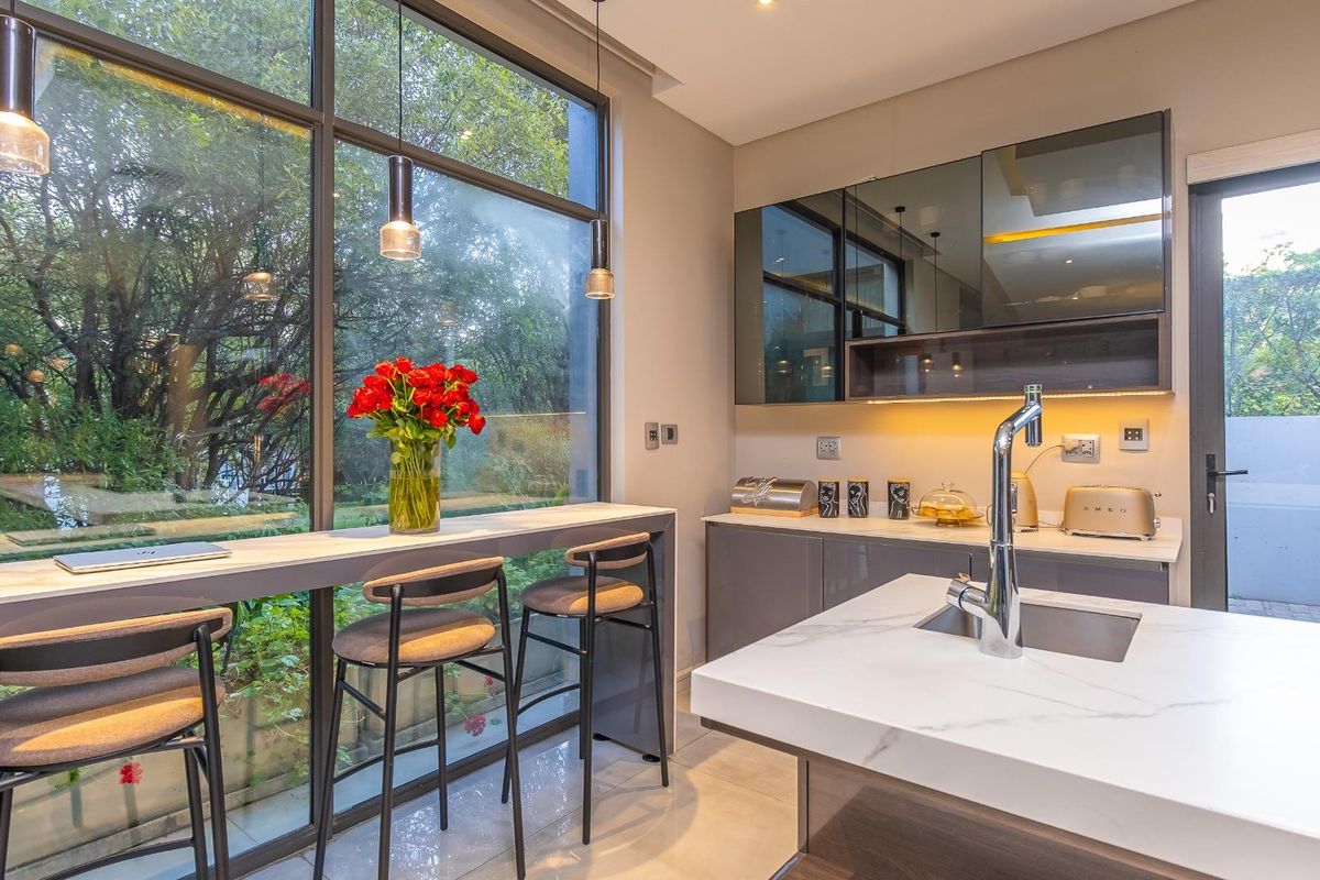 Modern kitchen featuring high-gloss cabinetry, marble-look stone countertops, an undermount sink with a gooseneck faucet, and floor-to-ceiling windows overlooking the garden.