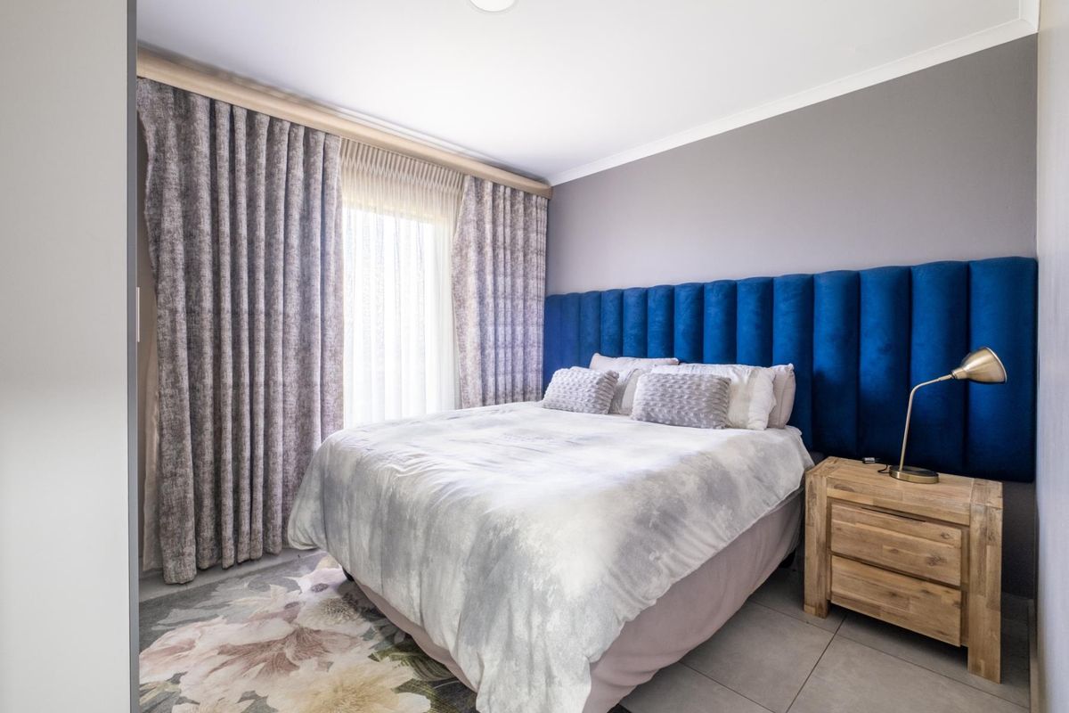 A well-maintained bedroom featuring tiled flooring, neutral wall tones, and floor-to-ceiling curtains providing natural light.
