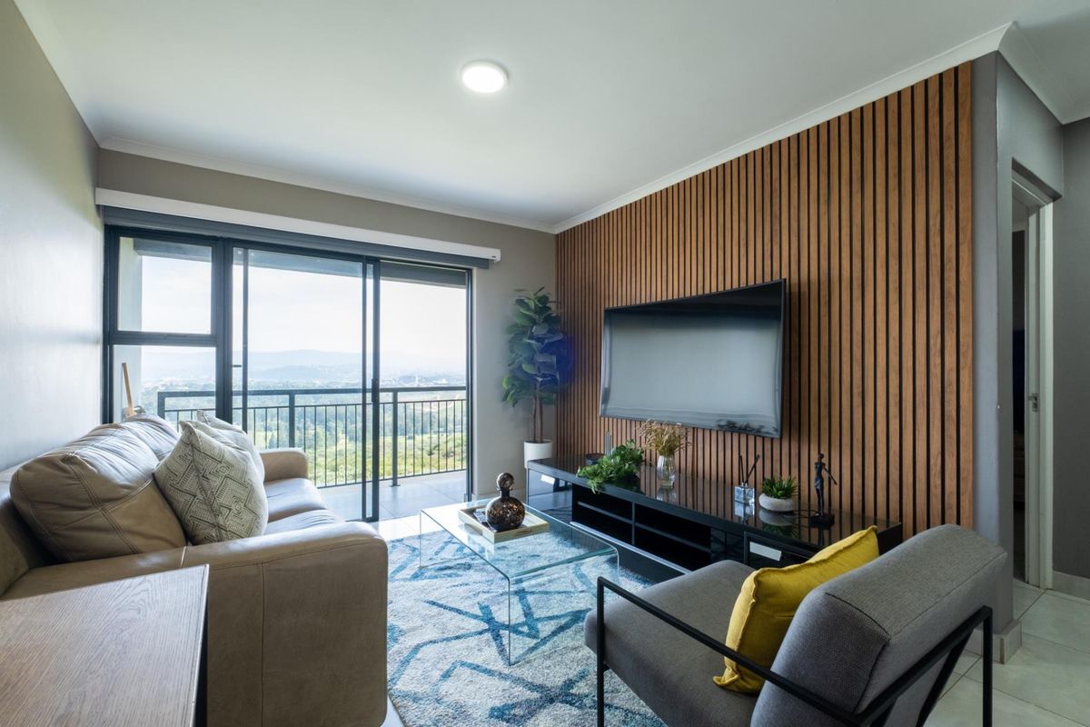 Modern living room featuring a decorative timber slat feature wall, tiled flooring, and large sliding glass doors opening to a balcony with scenic views.