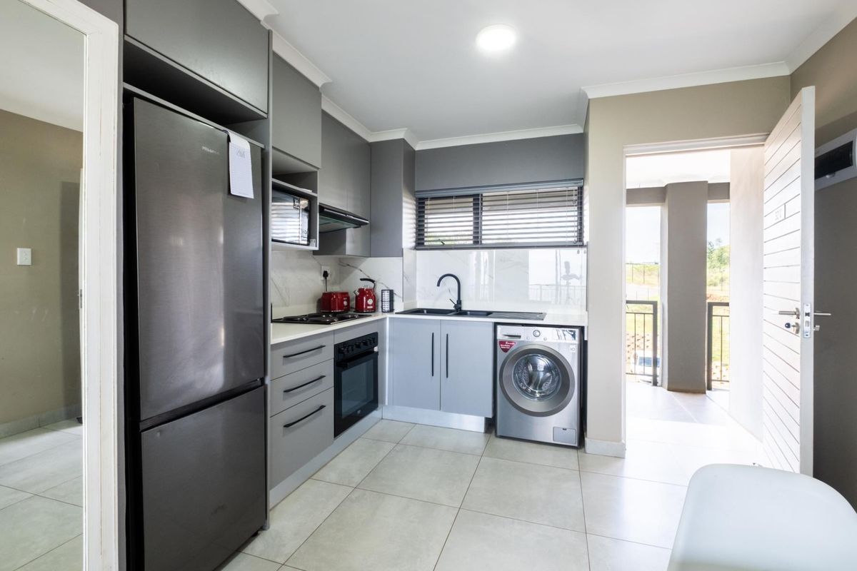 Modern kitchen featuring grey cabinetry, stone countertops, integrated oven, hob, extractor fan, and a dedicated space for a washing machine.